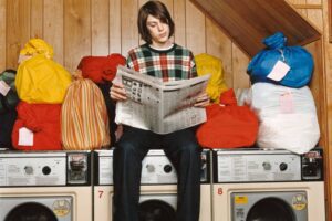 A person standing on top of a laundry machine while reading the paper