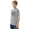 A boy standing in front of a wall wearing jeans and a t-shirt.