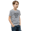 A boy standing in front of a wall wearing jeans and a t-shirt.