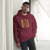 A man standing in front of a pillar wearing a maroon hoodie.