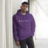 A man leaning against the wall wearing a purple hoodie.