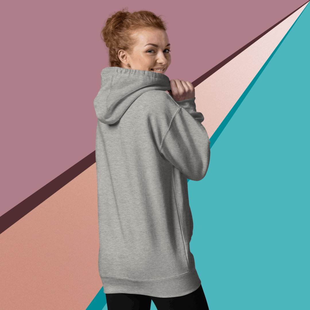 cotton-heritage-m2580-i-unisex-premium-pullover-hoodie-carbon-grey-back-68f046de06277 Woman in a gray hoodie posing against a colorful geometric background.