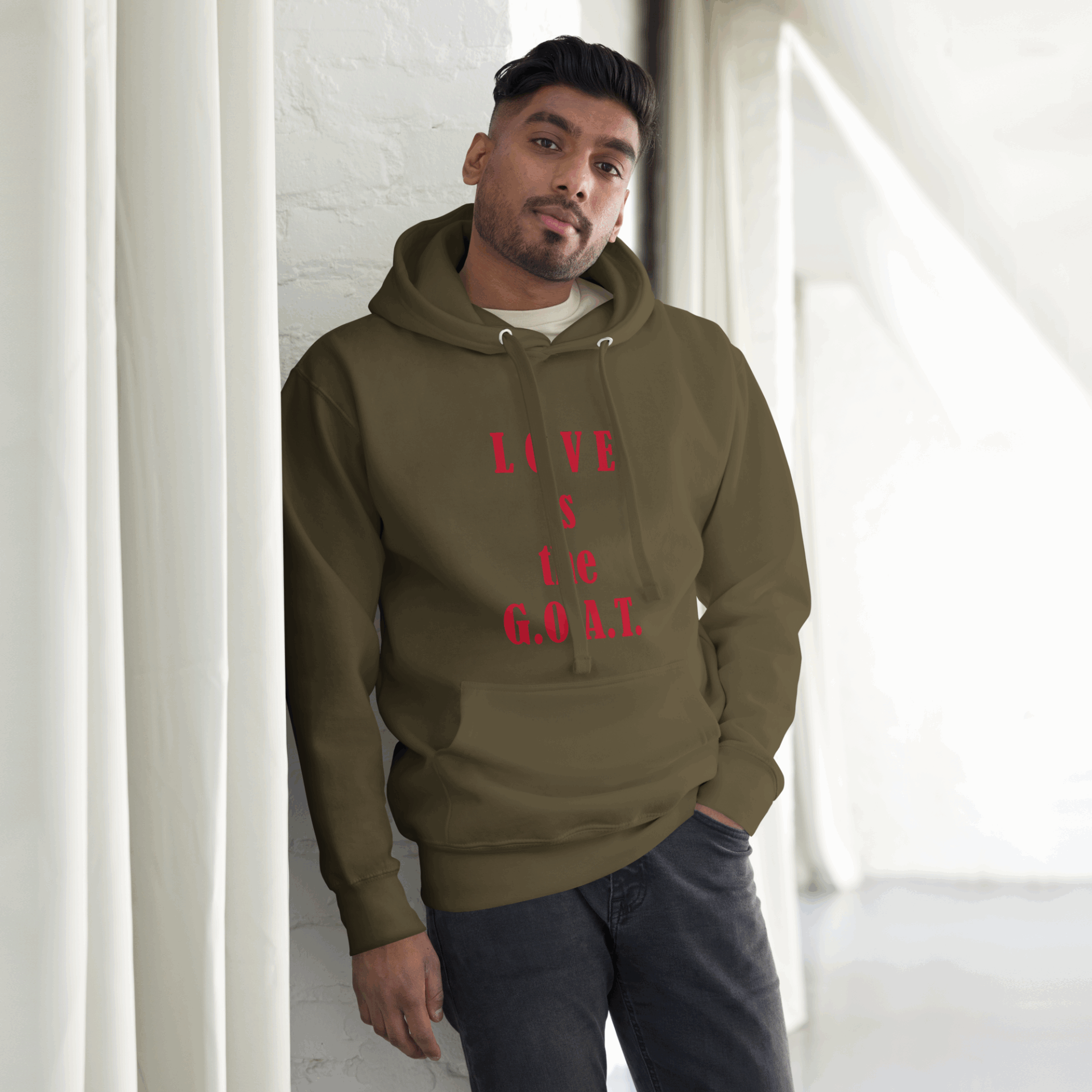 Man wearing an olive green hoodie with red text, standing by a bright window.