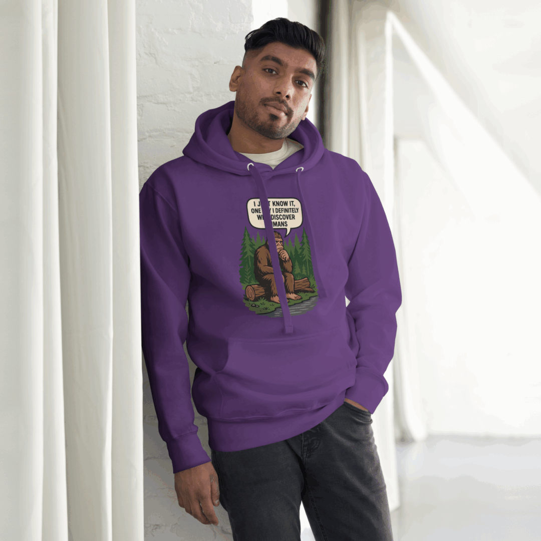 A man wearing a purple hoodie with a graphic design stands indoors near a window.