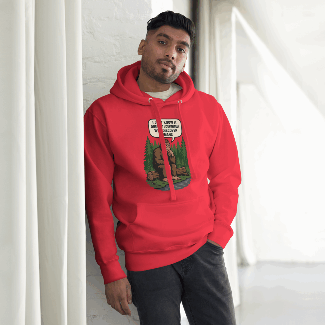 A man in a red hoodie with a graphic print stands by a window.
