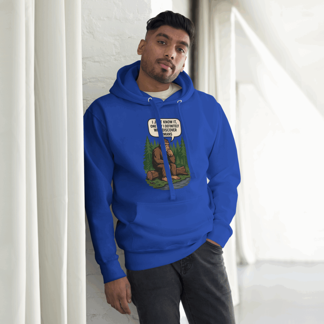 Man in a blue hoodie leaning against a white wall.