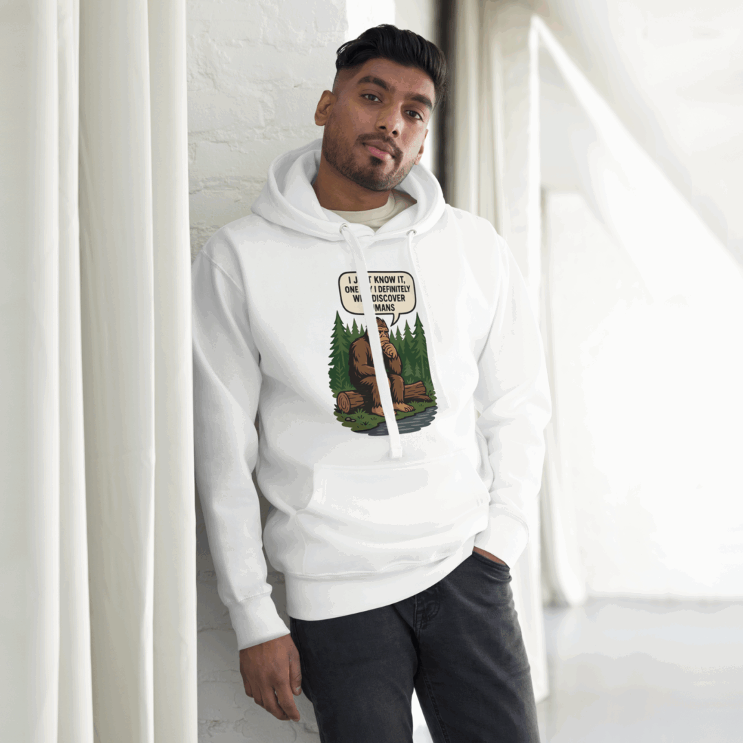 Man wearing a white hoodie with a graphic design, leaning against a white wall.