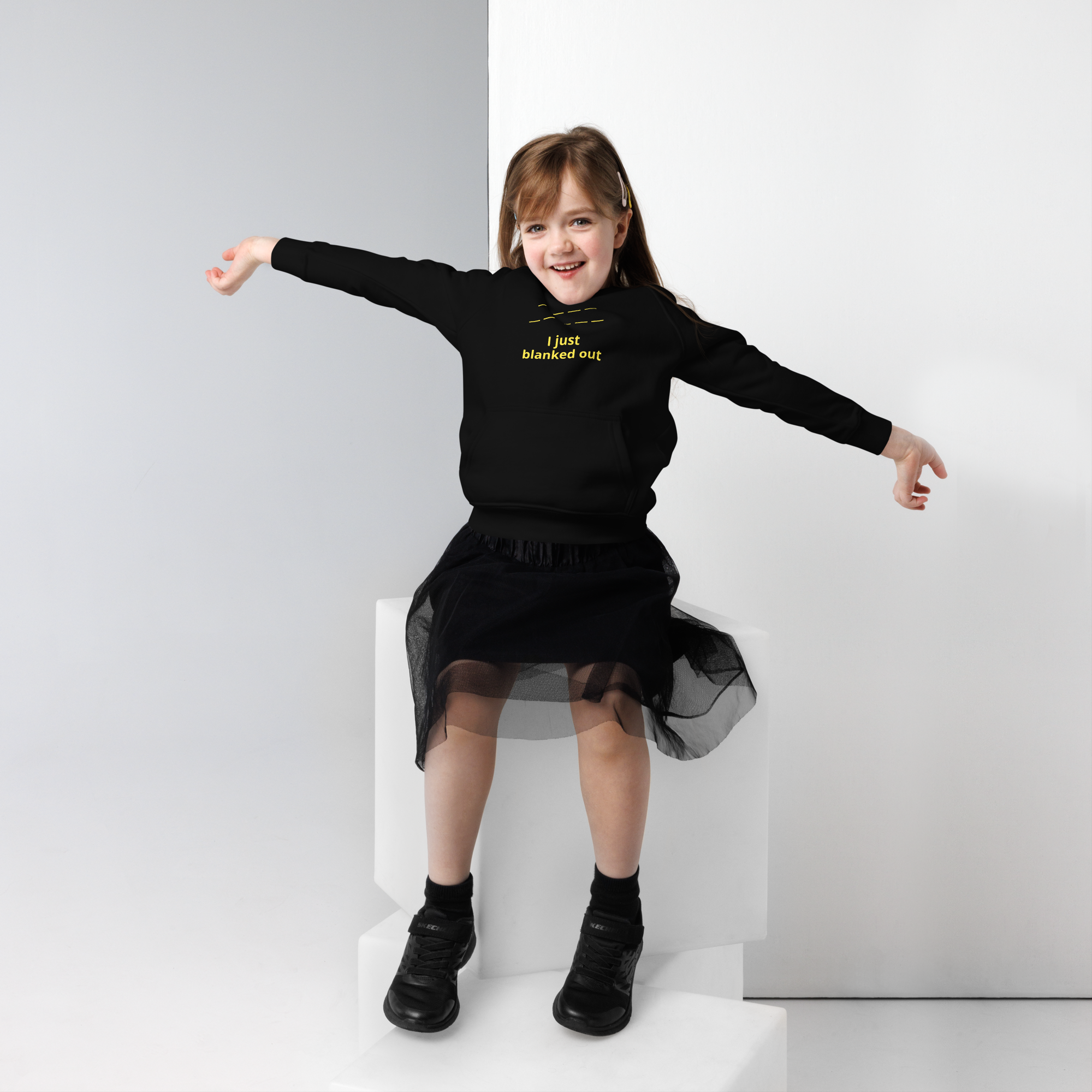 Smiling girl in black hoodie and skirt sitting with arms outstretched.