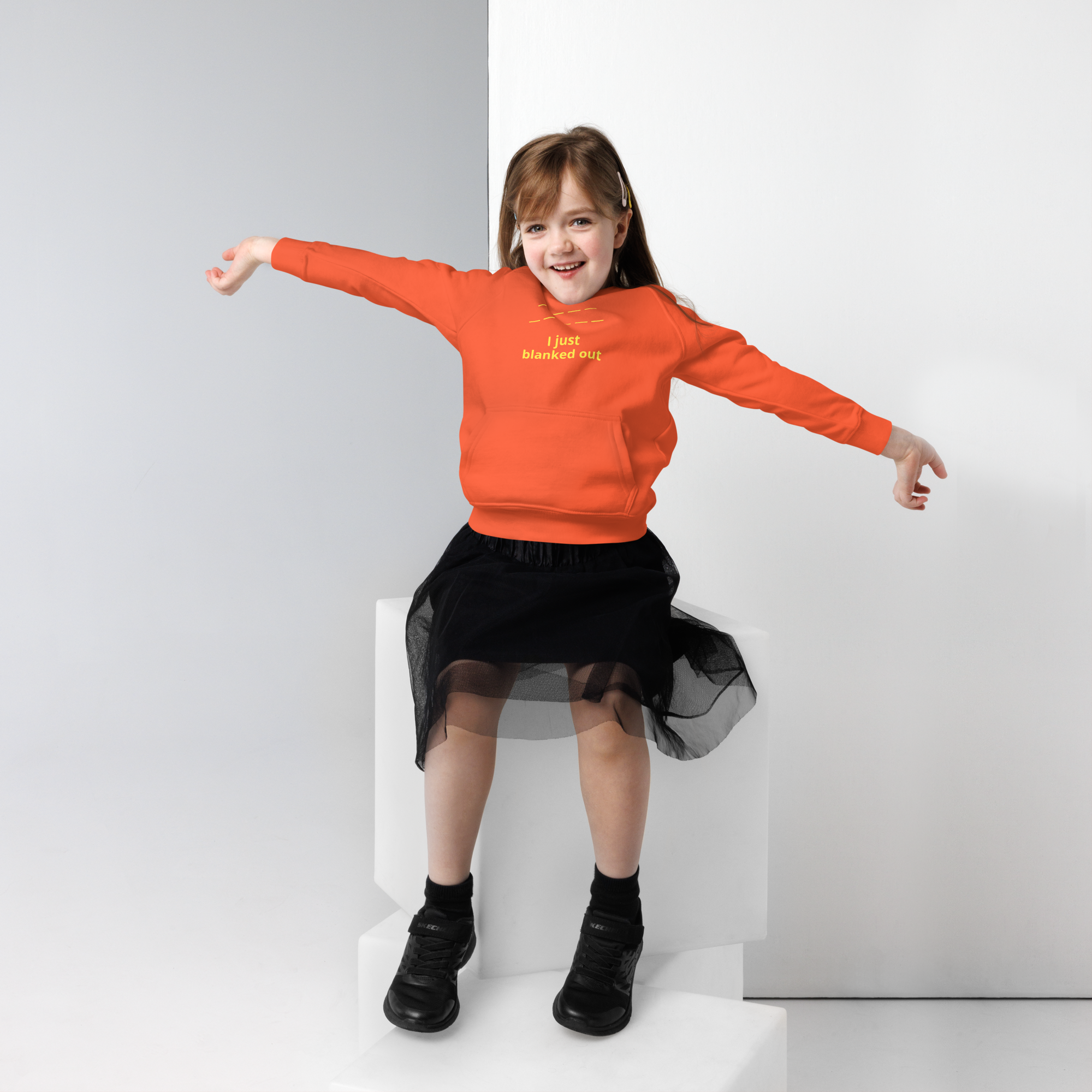 Happy girl in an orange sweatshirt and black skirt with arms outstretched.