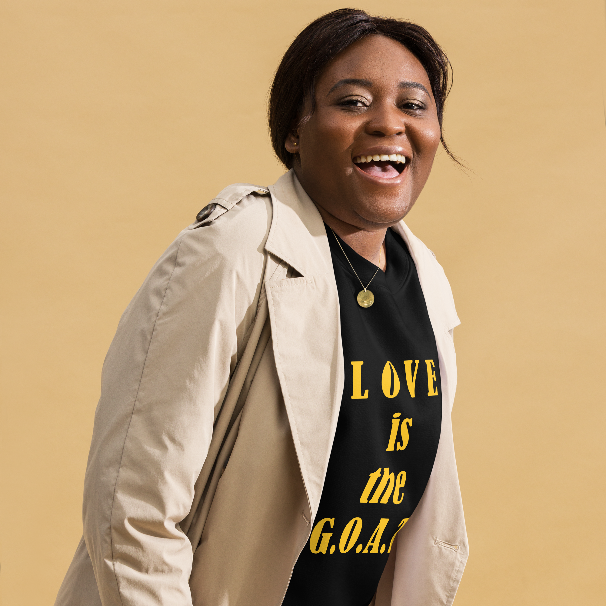 Smiling woman in beige coat and black T-shirt with yellow text.