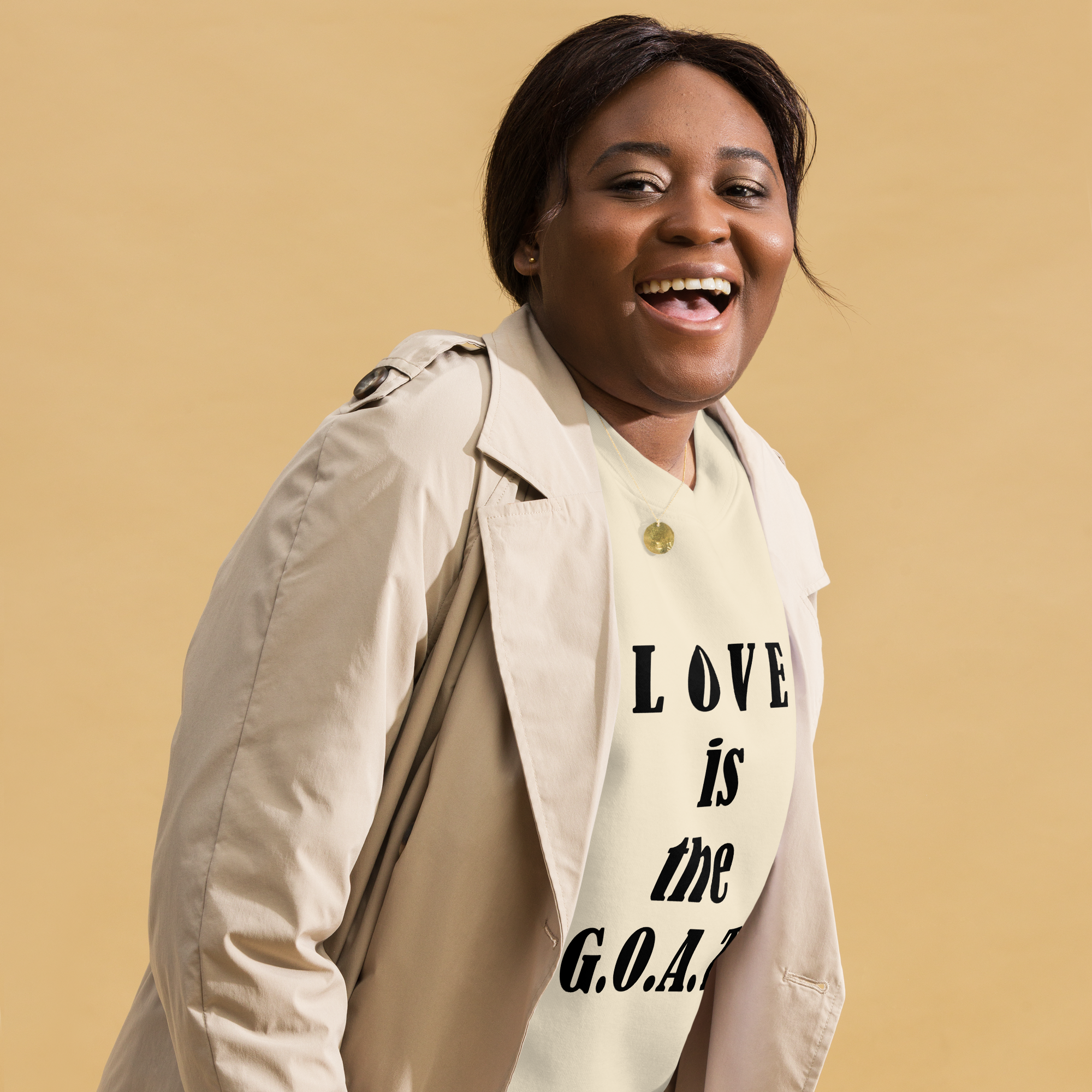 Smiling woman wearing a beige coat and a shirt that says "LOVE is the G.O.A.T."