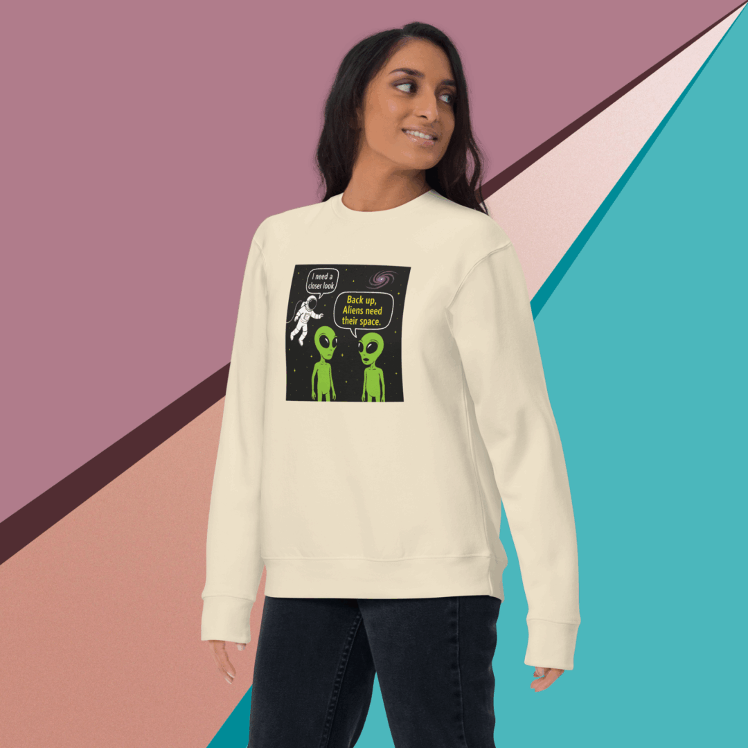 Woman wearing a cream sweatshirt with green alien graphics and black pants.