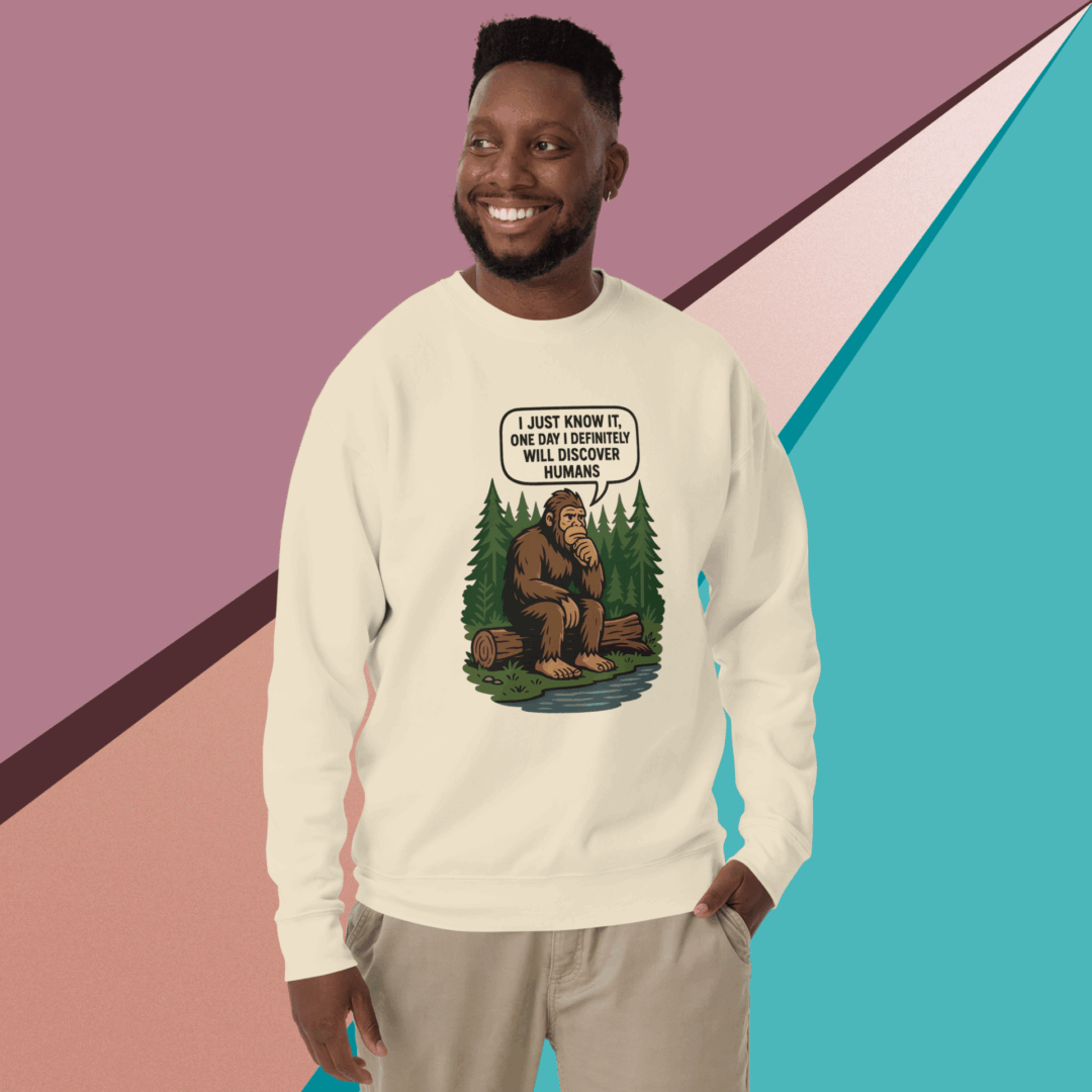 Smiling man wearing a beige sweatshirt with a graphic design, standing against a colorful geometric background.