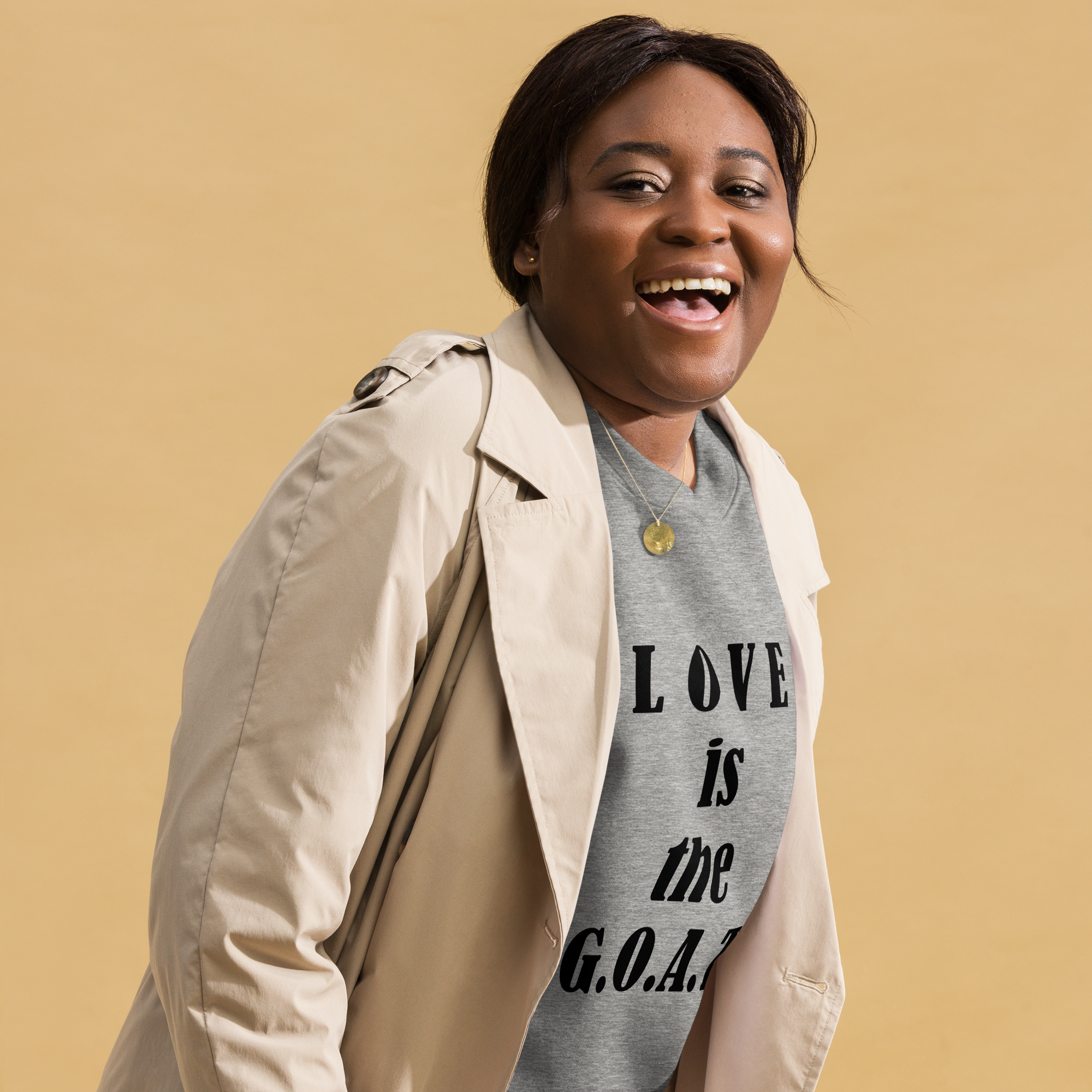 Happy woman wearing a beige coat and a gray shirt with a motivational quote.