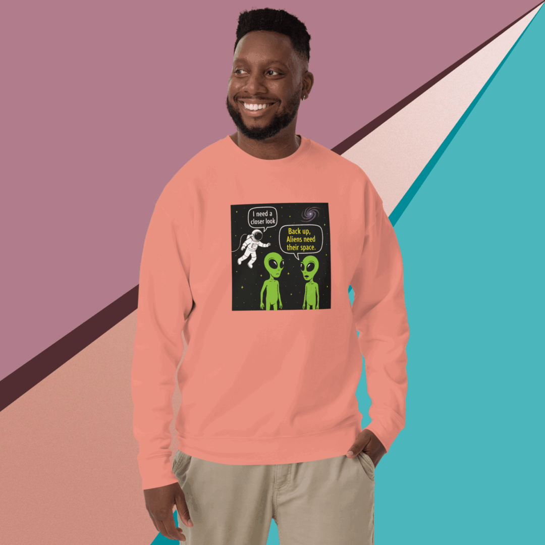 A man smiles wearing a peach sweatshirt with a science-themed graphic against a colorful geometric background.