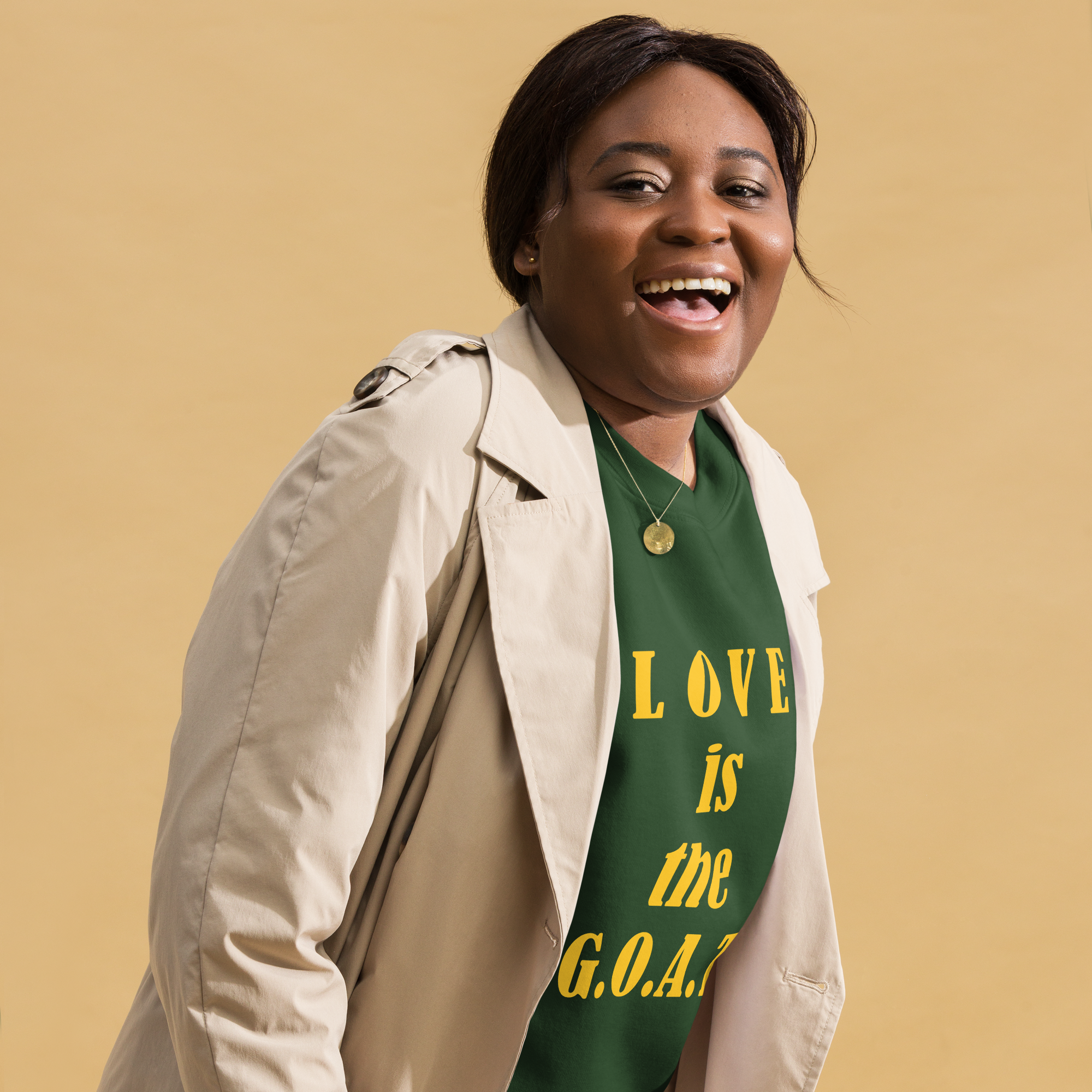 Smiling woman wearing a green shirt that says "LOVE is the G.O.A.T." with a beige coat.