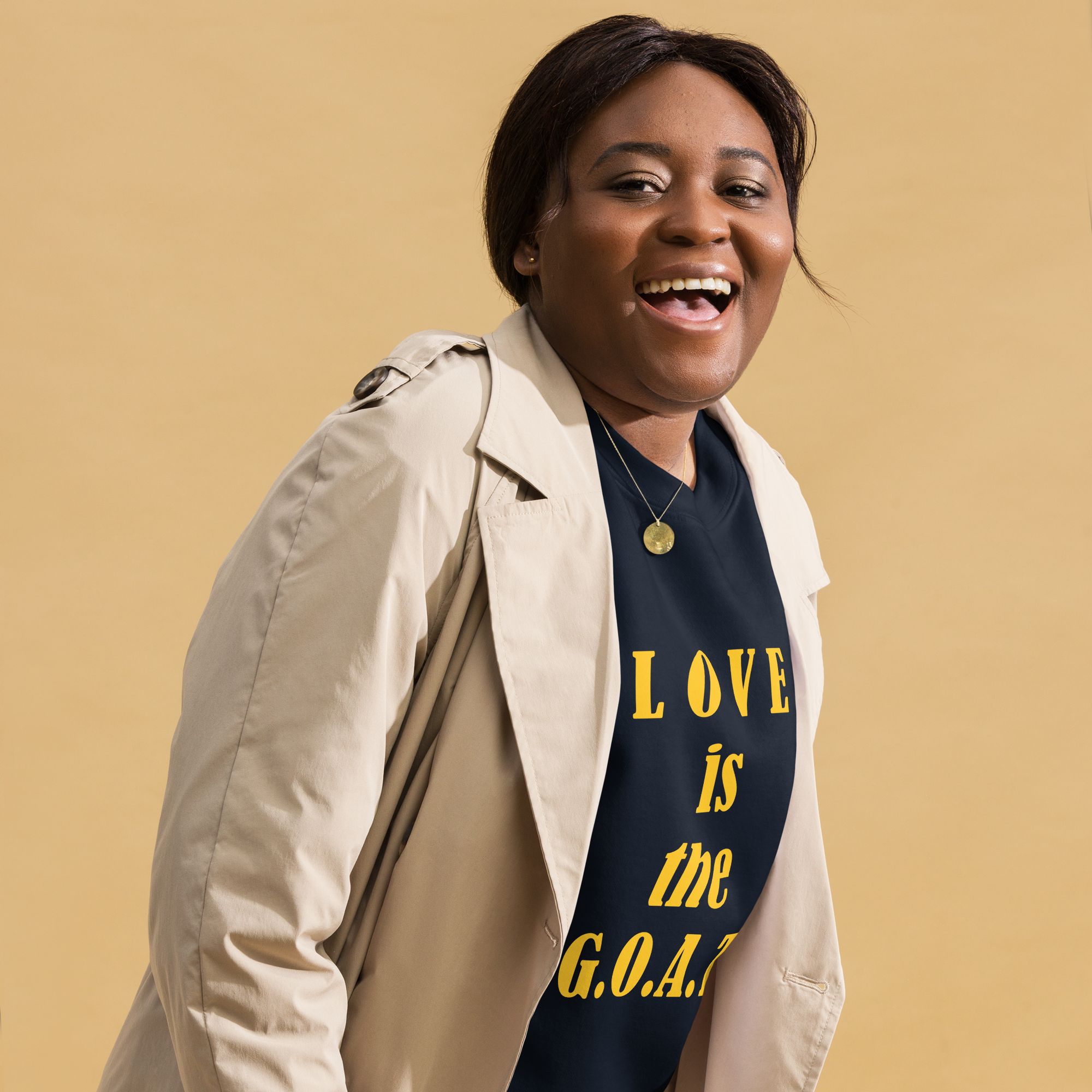 Smiling woman wearing a trench coat and a slogan T-shirt that says 'LOVE is the G.O.A.T.'