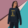unisex-premium-sweatshirt-navy-blazer-front-68f061abc7e68 Woman wearing a black sweatshirt with the phrase 'LOVE IS the G.O.A.T.'