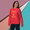 unisex-premium-sweatshirt-team-red-front-68f061abccdbe Woman wearing a red sweatshirt with "Love is the G.O.A.T." text.