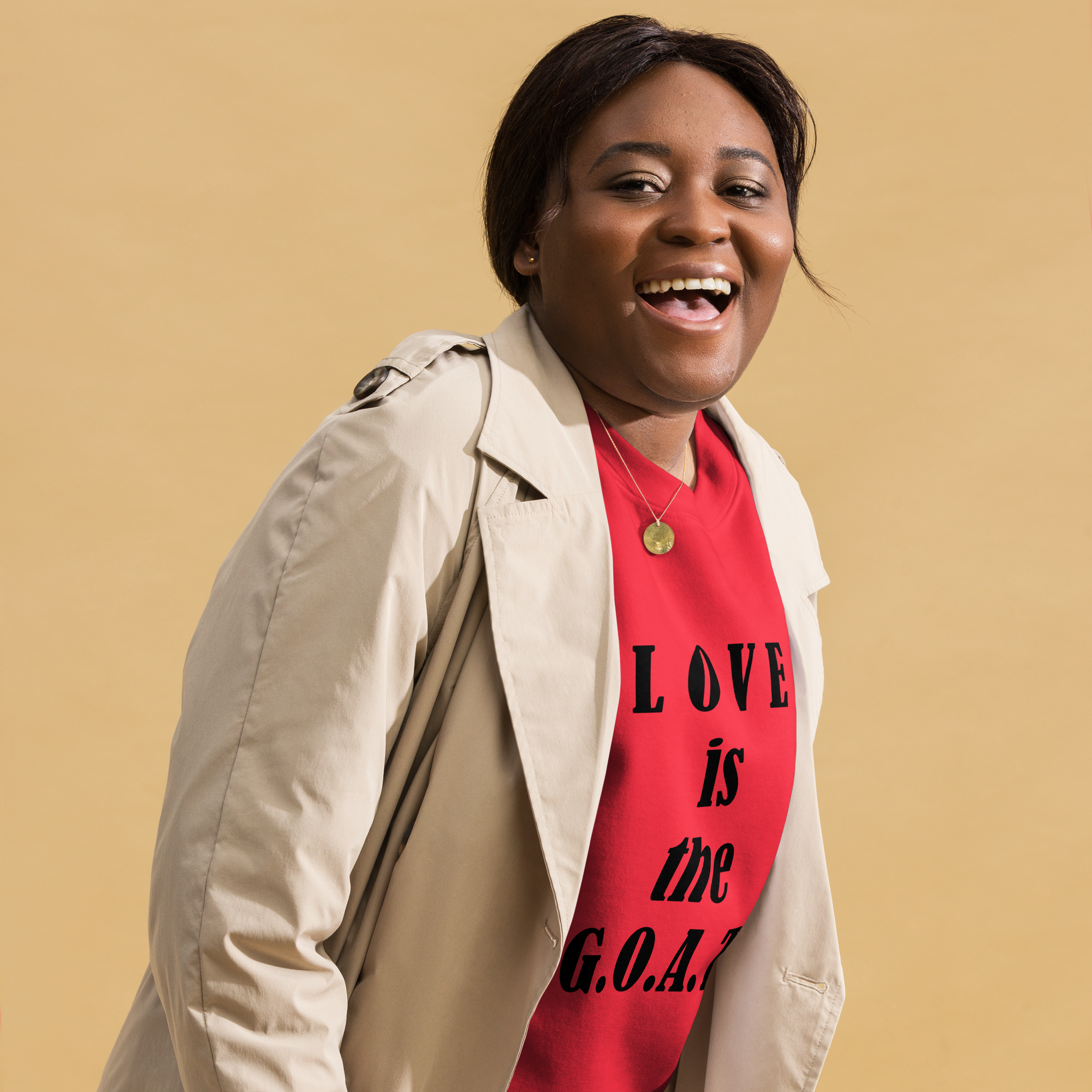 Happy woman in beige coat and red shirt with 'LOVE is the G.O.A.T' text.