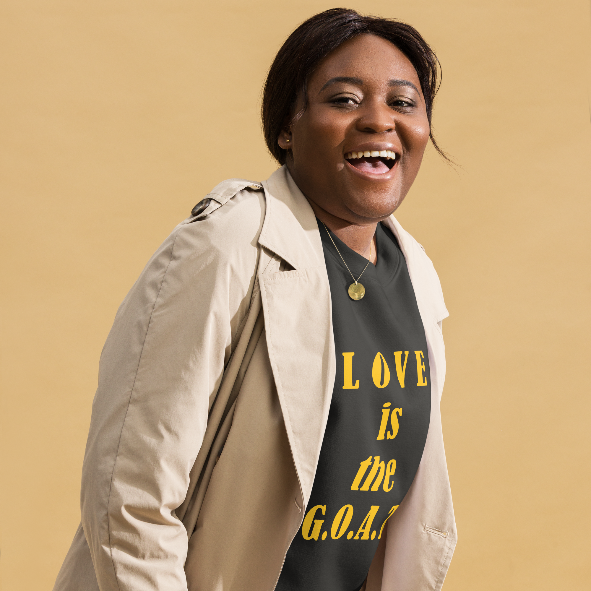 Smiling woman wearing a beige trench coat and a black shirt with yellow text.