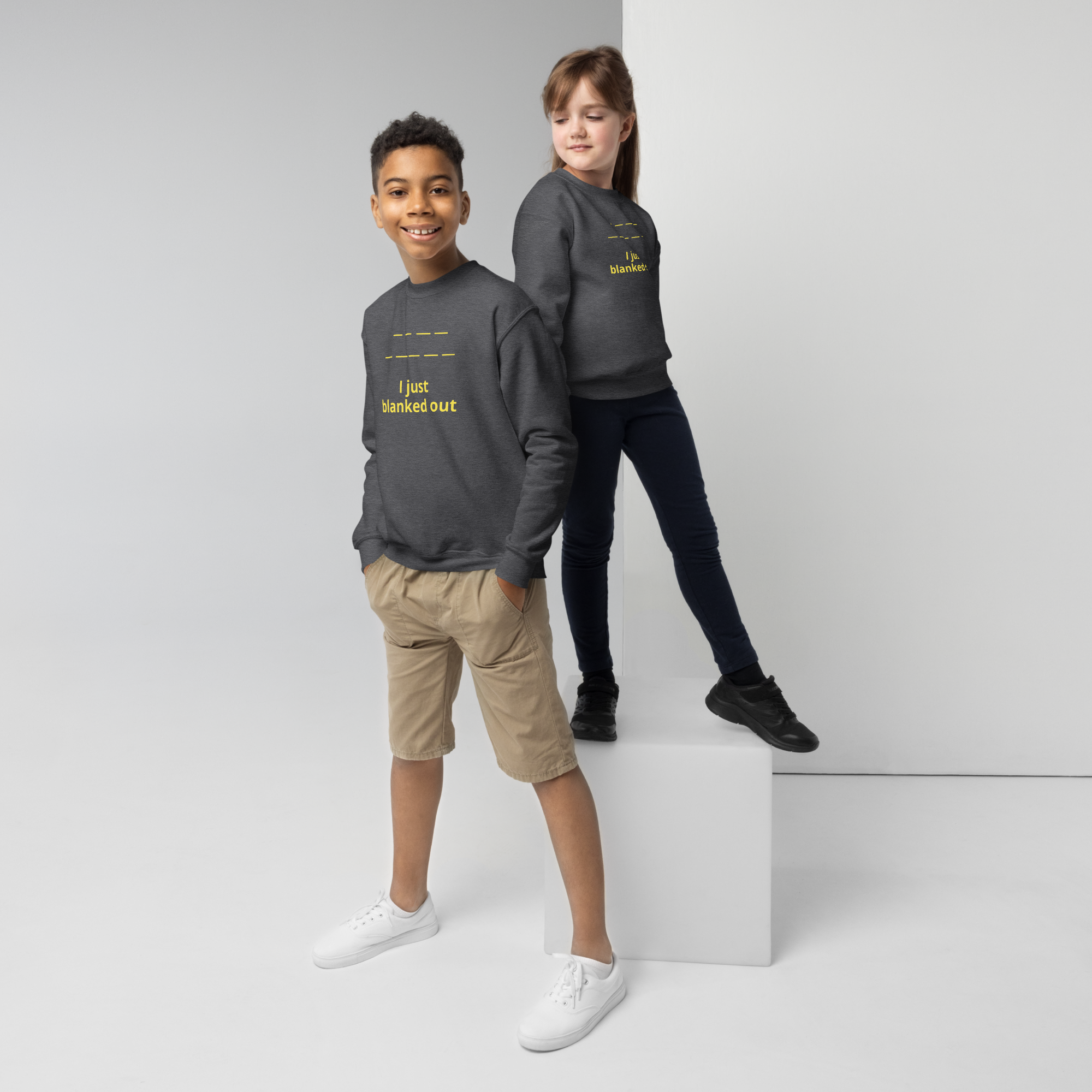 Two children wearing matching dark gray sweatshirts with yellow text, posing confidently in a studio.