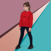 Young girl in a red sweater and black pants posing against a colorful geometric background.