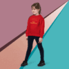Young girl in a red sweater standing confidently against a colorful geometric background.