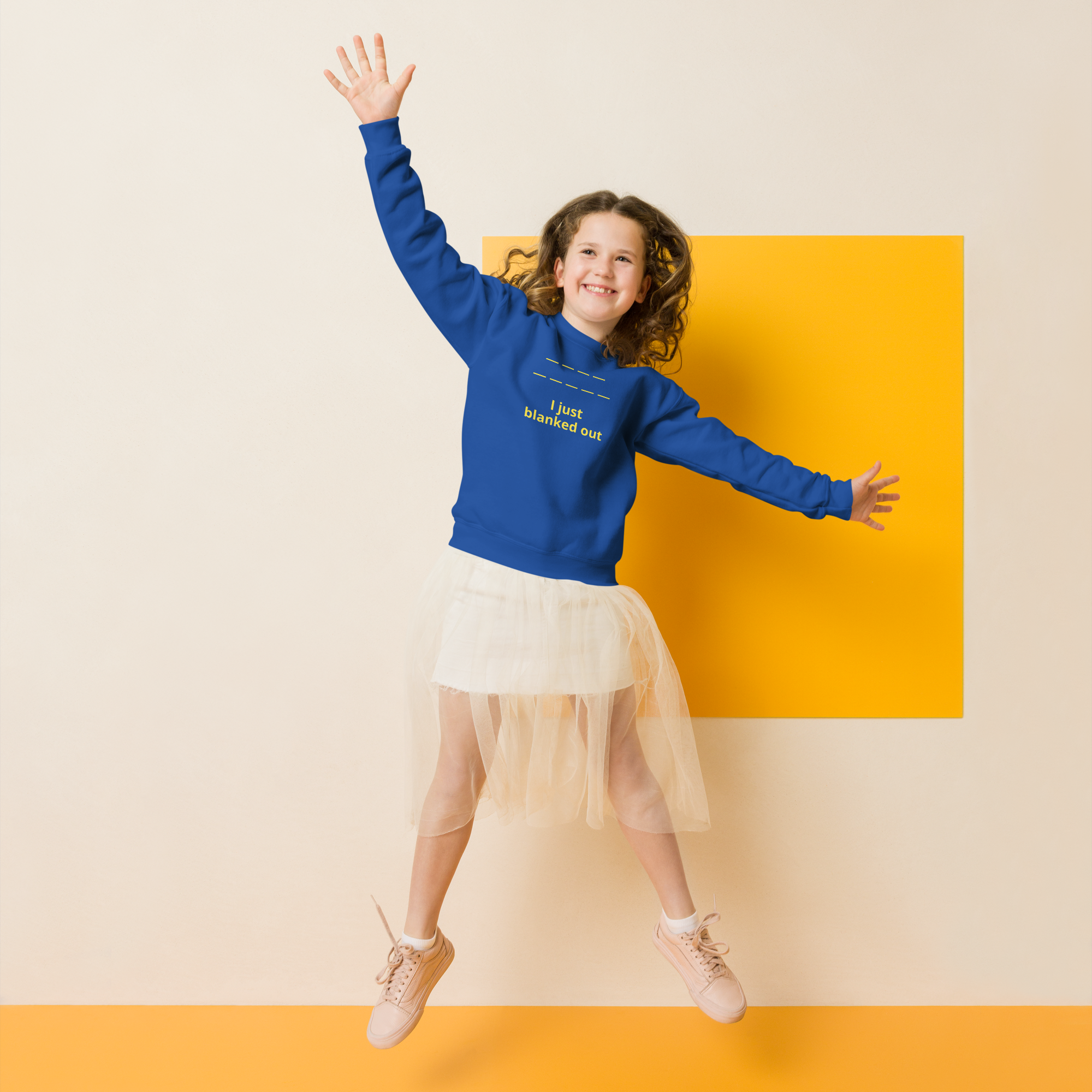 Joyful girl jumping with a bright blue sweatshirt and cream tulle skirt.