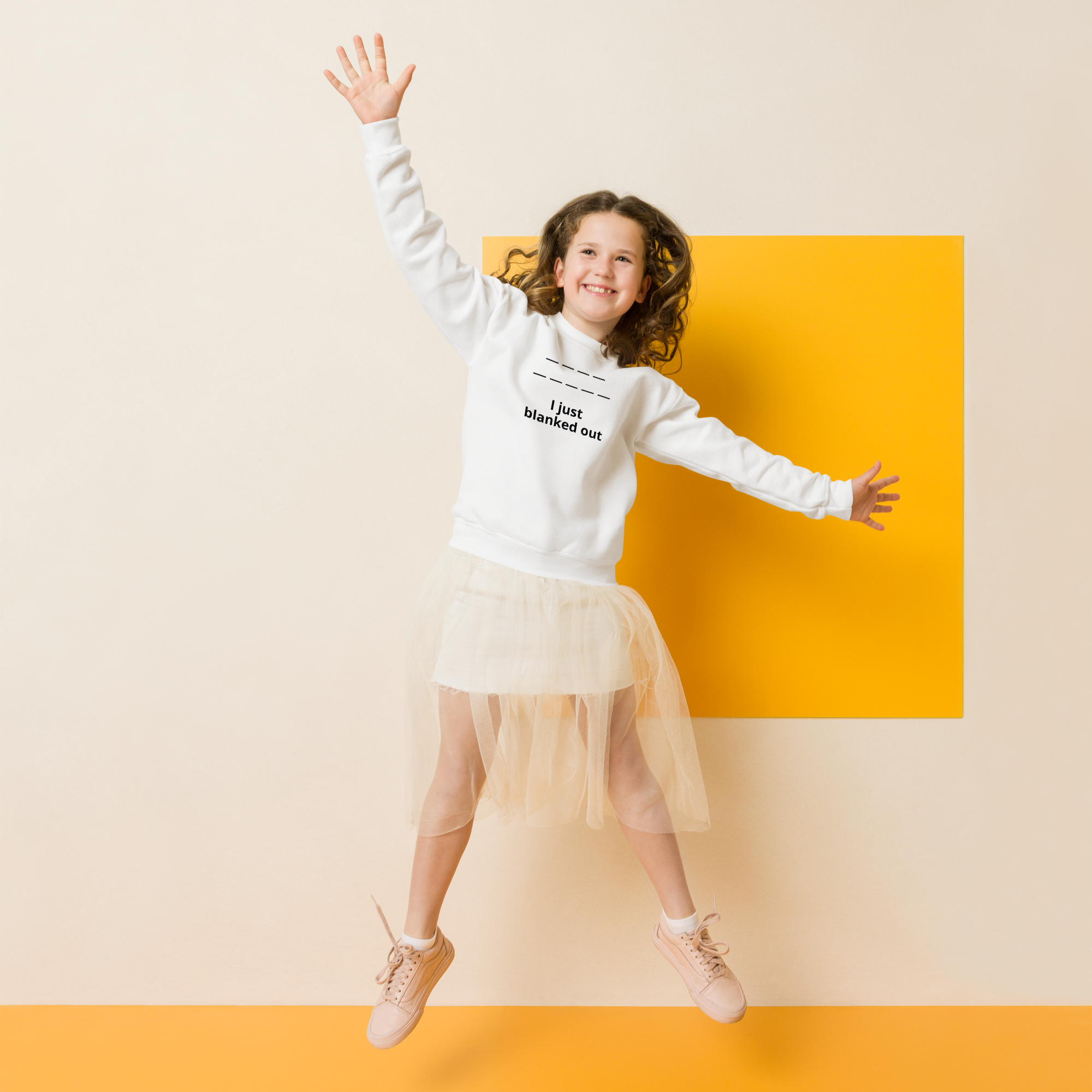 Joyful girl jumping in front of a yellow square, wearing a white sweatshirt.