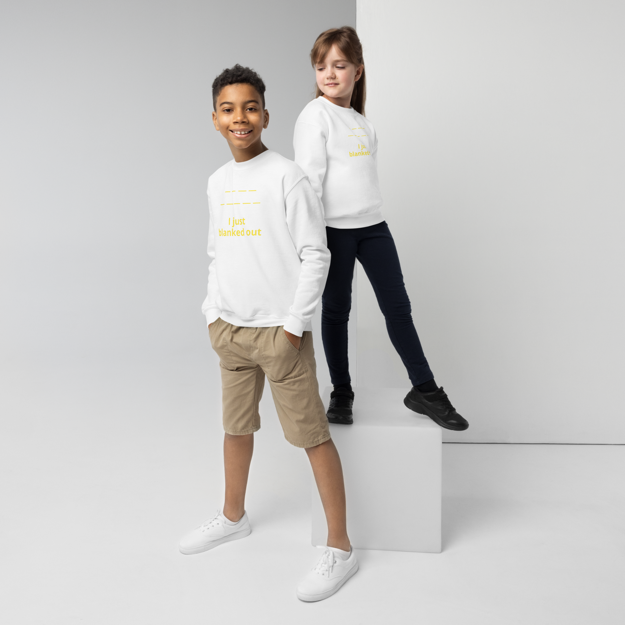 Two kids wearing white sweatshirts with yellow text, posing against a plain backdrop.