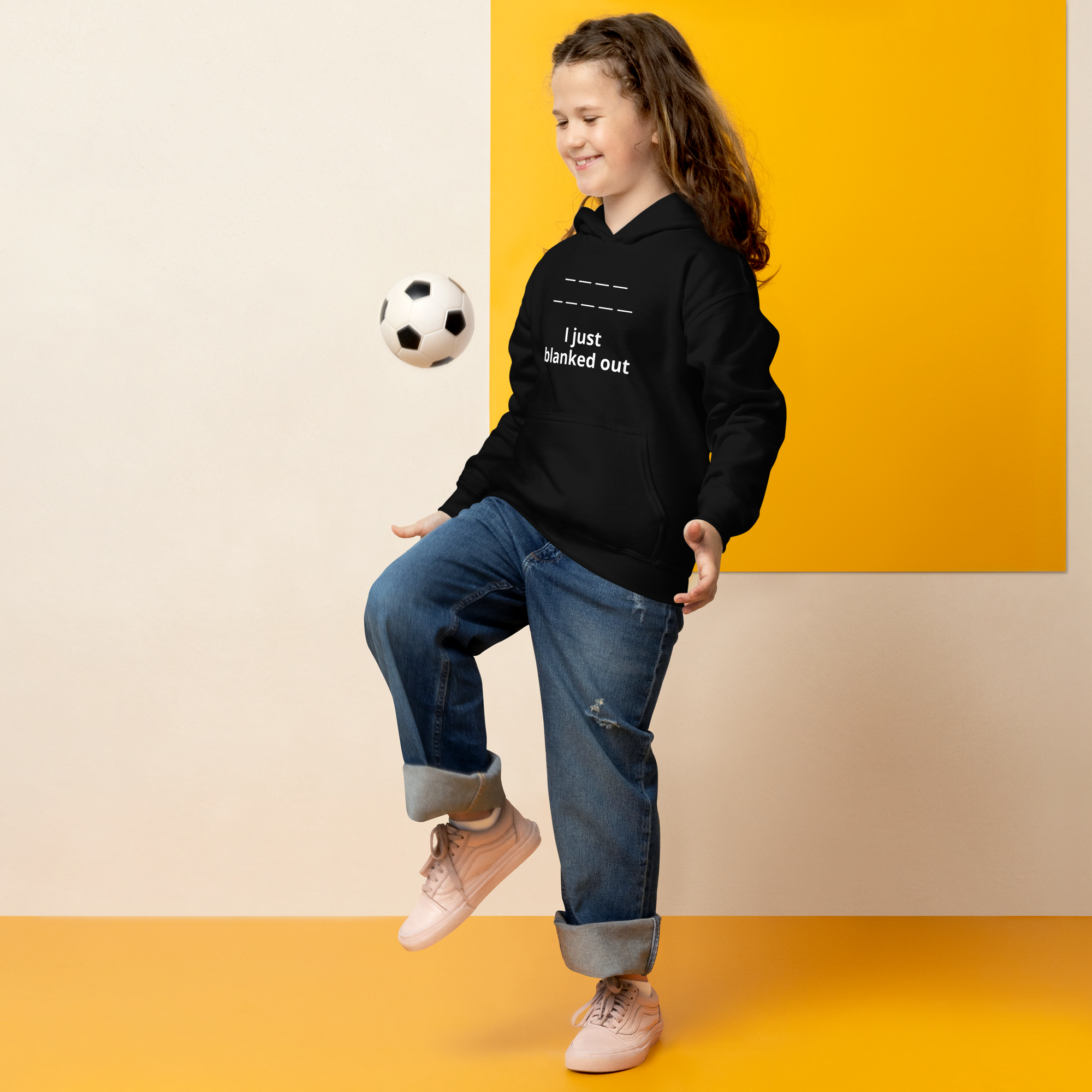 A girl in a black hoodie playing soccer indoors with a smile.