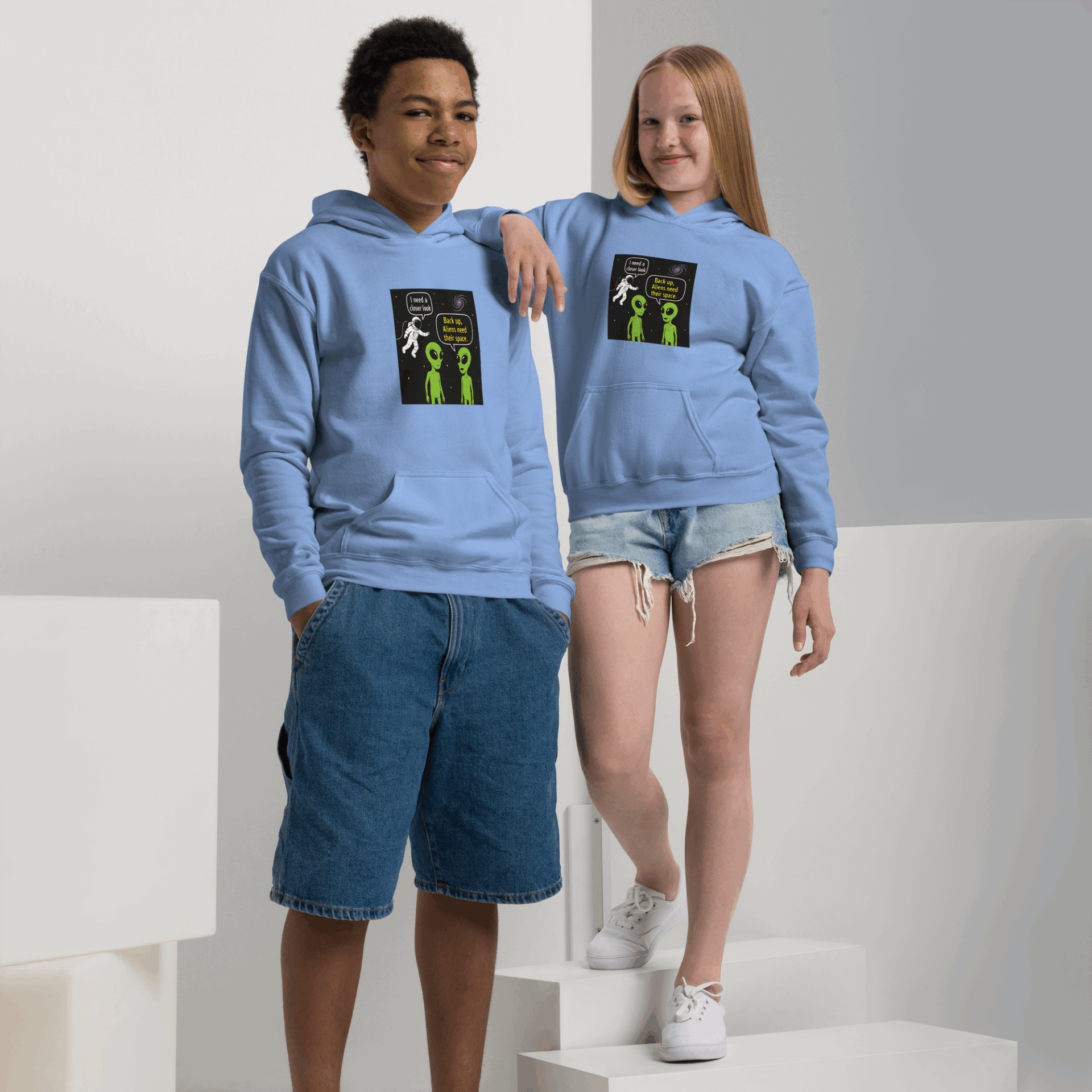 Two kids wearing matching light blue hoodies with a space-themed alien comic print.