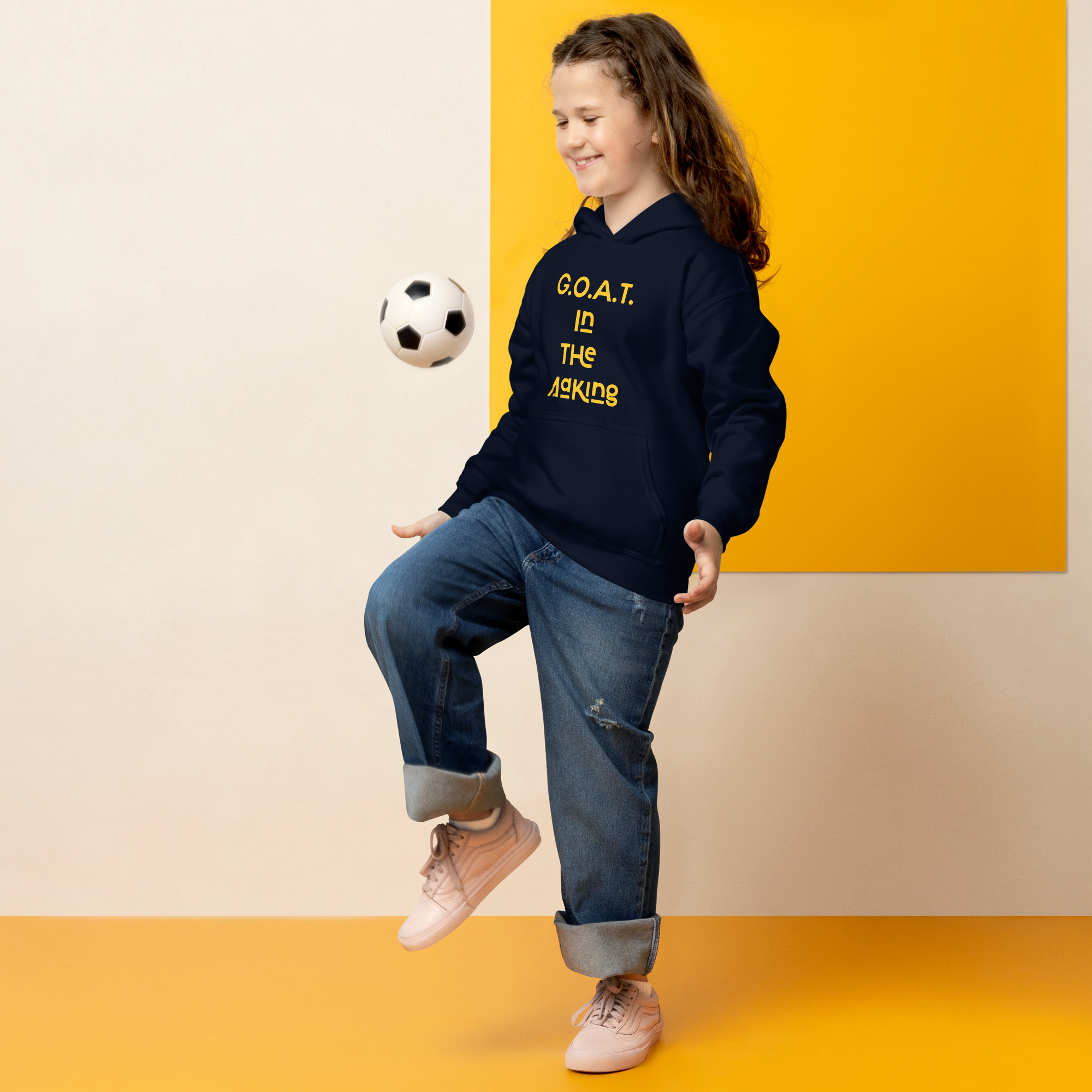 Young girl joyfully playing soccer, wearing a navy hoodie with a motivational slogan.