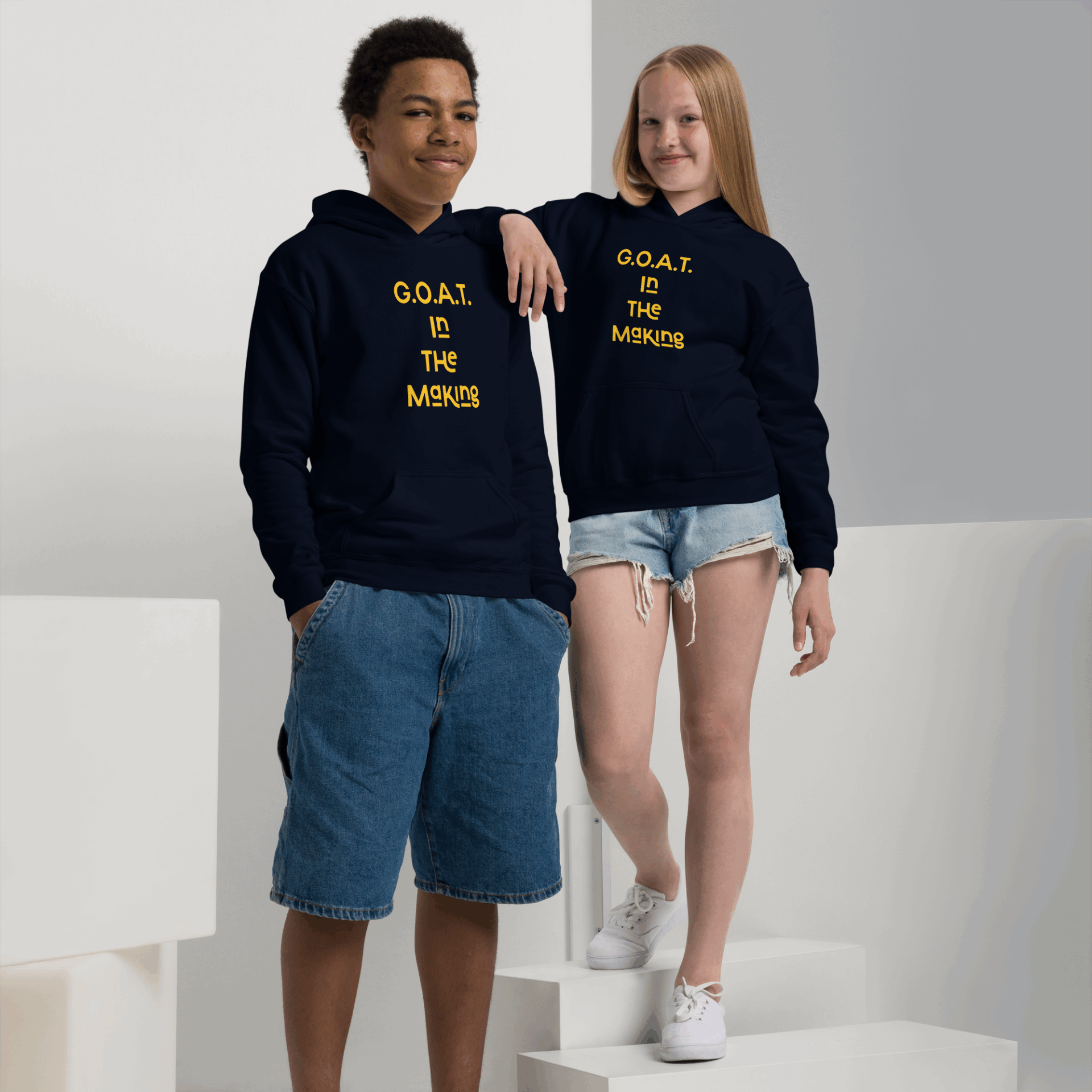 Two teenagers wearing navy hoodies with 'G.O.A.T. In The Making' in yellow lettering.