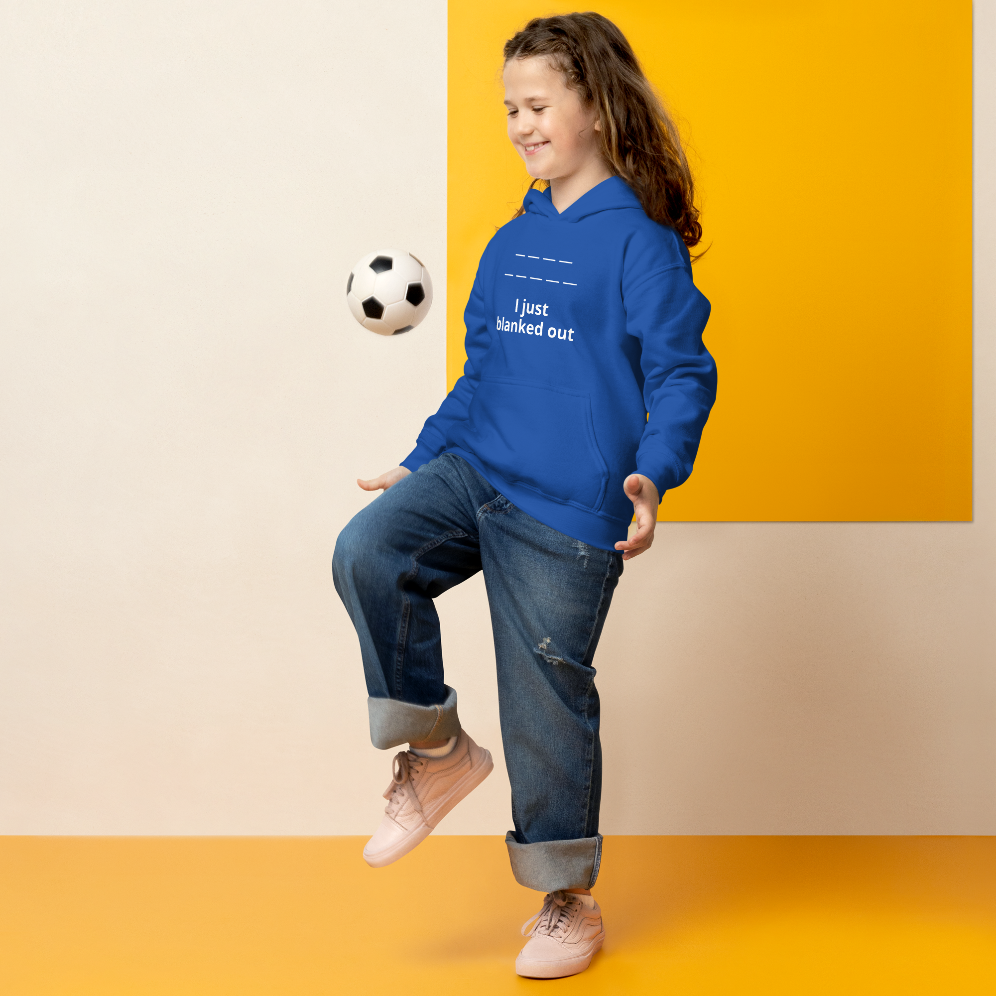 A smiling girl in a blue hoodie plays soccer indoors.