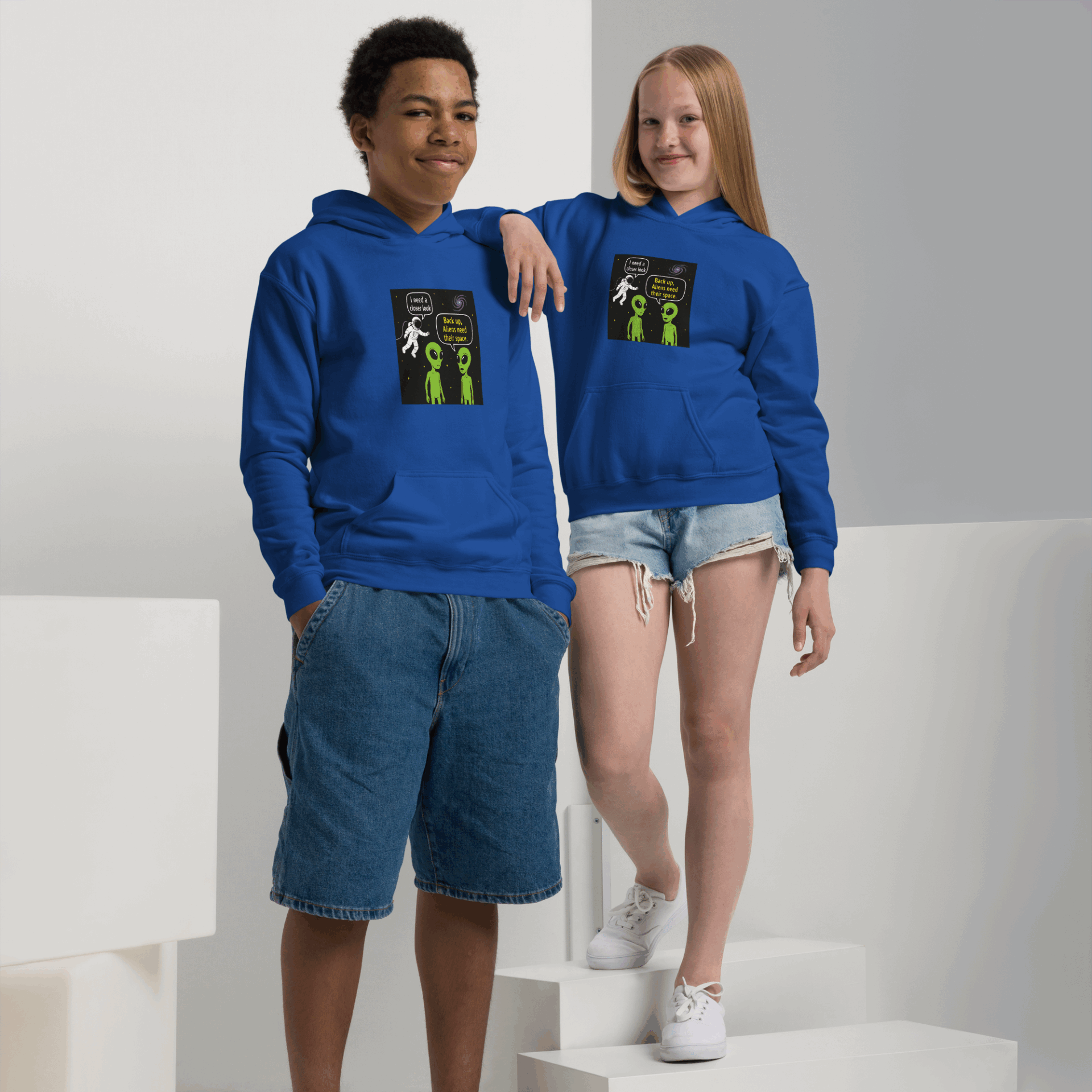 Two kids wearing matching blue hoodies with an alien comic design.