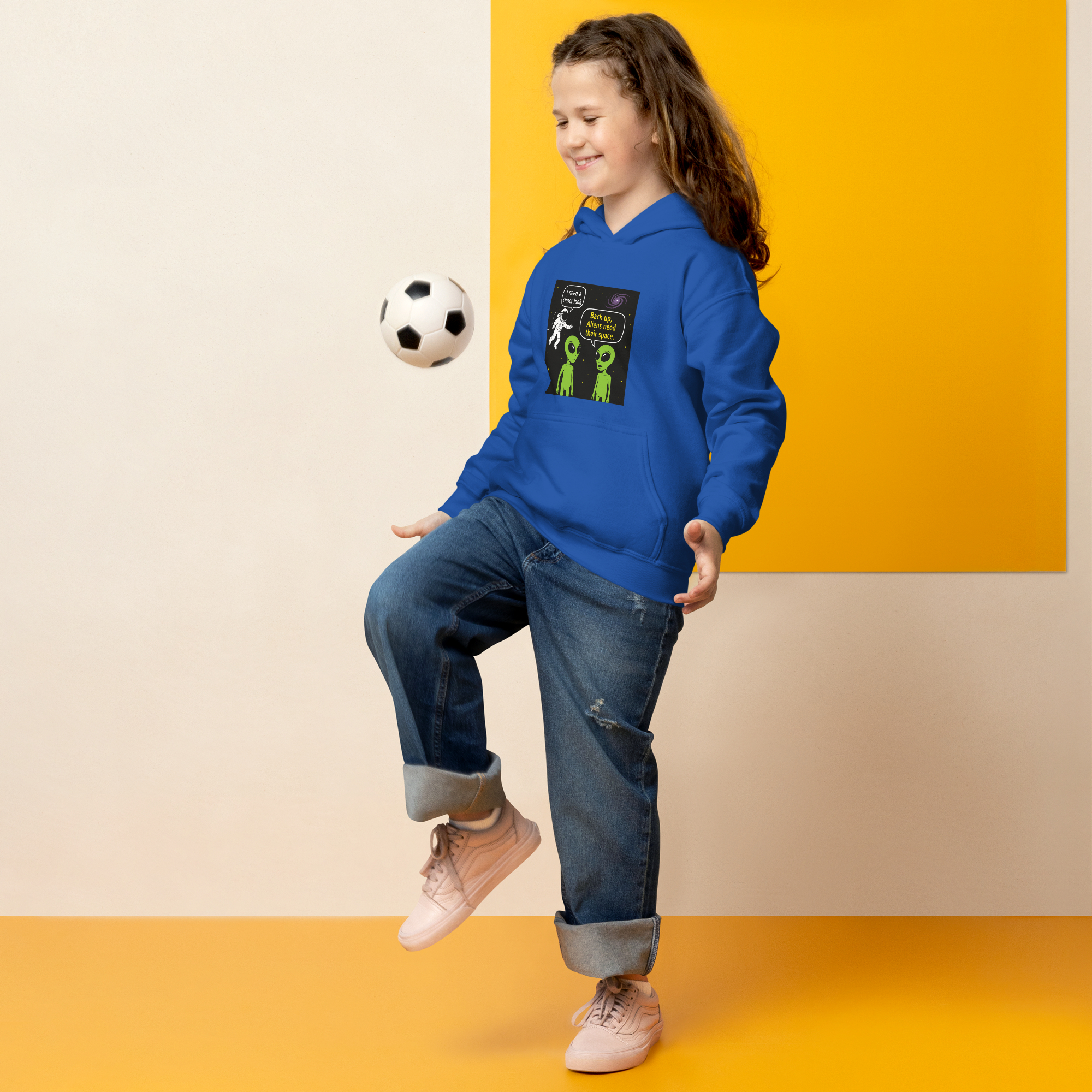 Girl in blue hoodie playing soccer with a humorous alien-themed design.