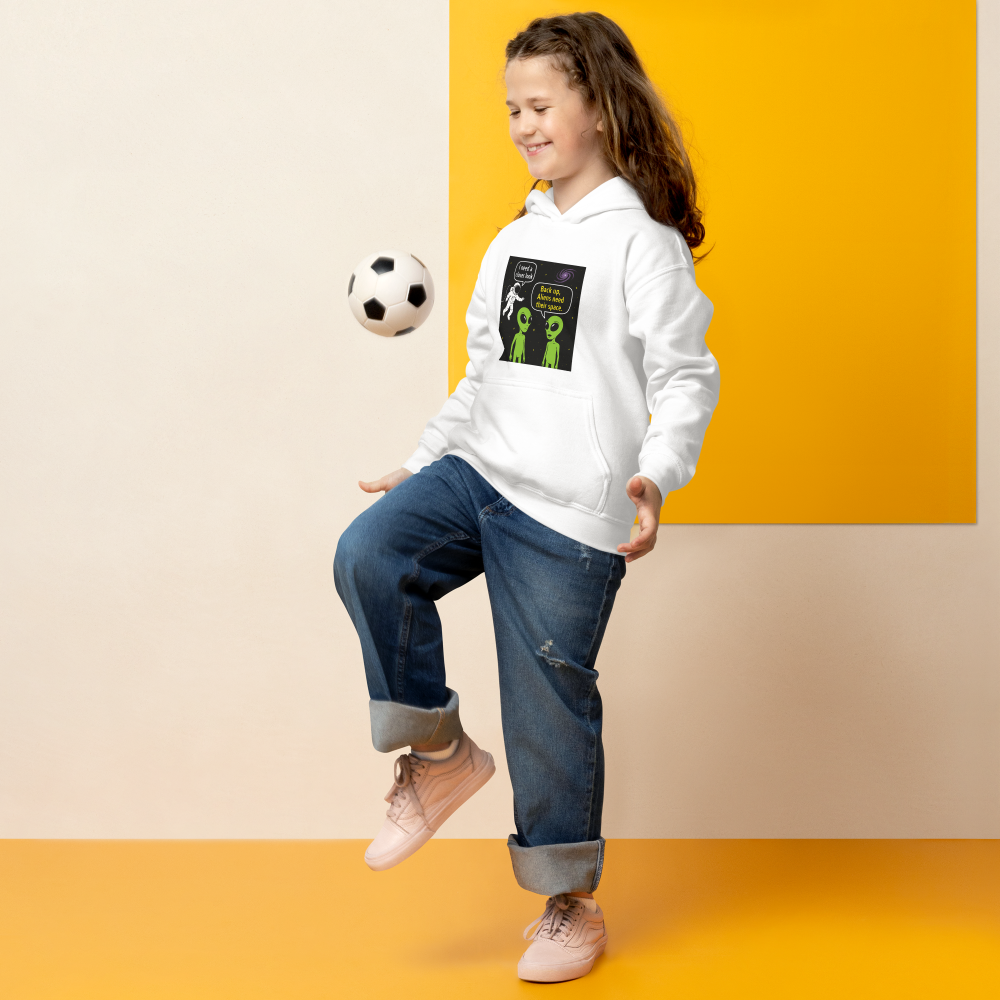 Smiling girl in white hoodie playing soccer with alien-themed design on hoodie.